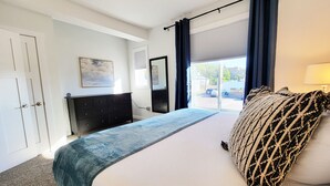 A bedroom with a bed, a dresser, a mirror, a window with curtains, and a painting on the wall. - Stay Lincoln Park 1 | Craft District Condo (Duluth)