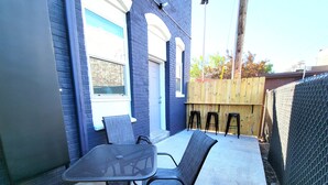 An outdoor patio with a table and two chairs, a wooden fence, and a brick wall. - Stay Lincoln Park 1 | Craft District Condo (Duluth)