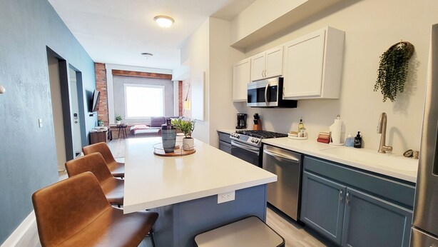 A modern kitchen with a central island, stainless steel appliances, and a seating area with a view to the living room. - Stay Lincoln Park 1 | Craft District Condo (Duluth)