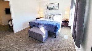 A hotel room with a bed, a bedside table, a chair, a flat-screen TV, and a window with curtains. - Craft District Pet-Friendly Condo by Heirloom (Duluth)