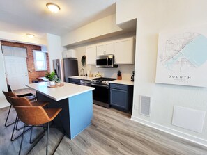 Een moderne keuken met witte kasten, een centraal eiland en een eethoek met twee stoelen.