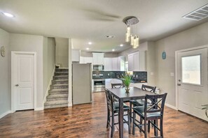 A modern kitchen with white cabinets, a dining area with a dark wooden table and chairs, and a staircase leading to another level. - Brand New! Fully Furnished Texas City Home (Houston)