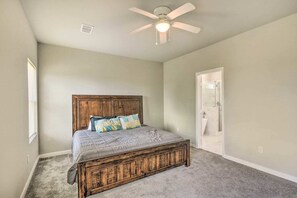 A bedroom with a wooden bed, a ceiling fan, and a door leading to a bathroom. - Brand New! Fully Furnished Texas City Home (Houston)