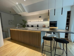 A modern kitchen with a central island, bar stools, a built-in oven, and pendant lighting. - Luxurious loft with large sun terrace and sauna (München)