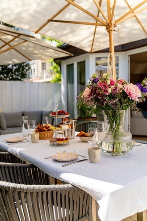 Un espace de restauration en plein air avec une table dressée pour un repas, un grand parasol et un vase rempli de fleurs.