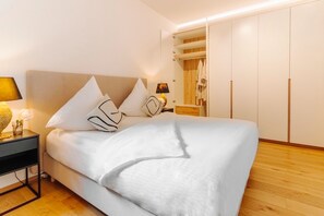Un lit bien fait, avec du linge de lit blanc, une lampe de chevet et une table de chevet sur laquelle se trouvent une lampe et un vase de fleurs.