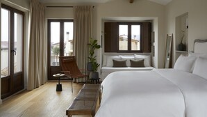 A hotel room with a large bed, a sitting area with a chair and a small table, a potted plant, and a view through a window. - The Storyteller House (Kalabaka)