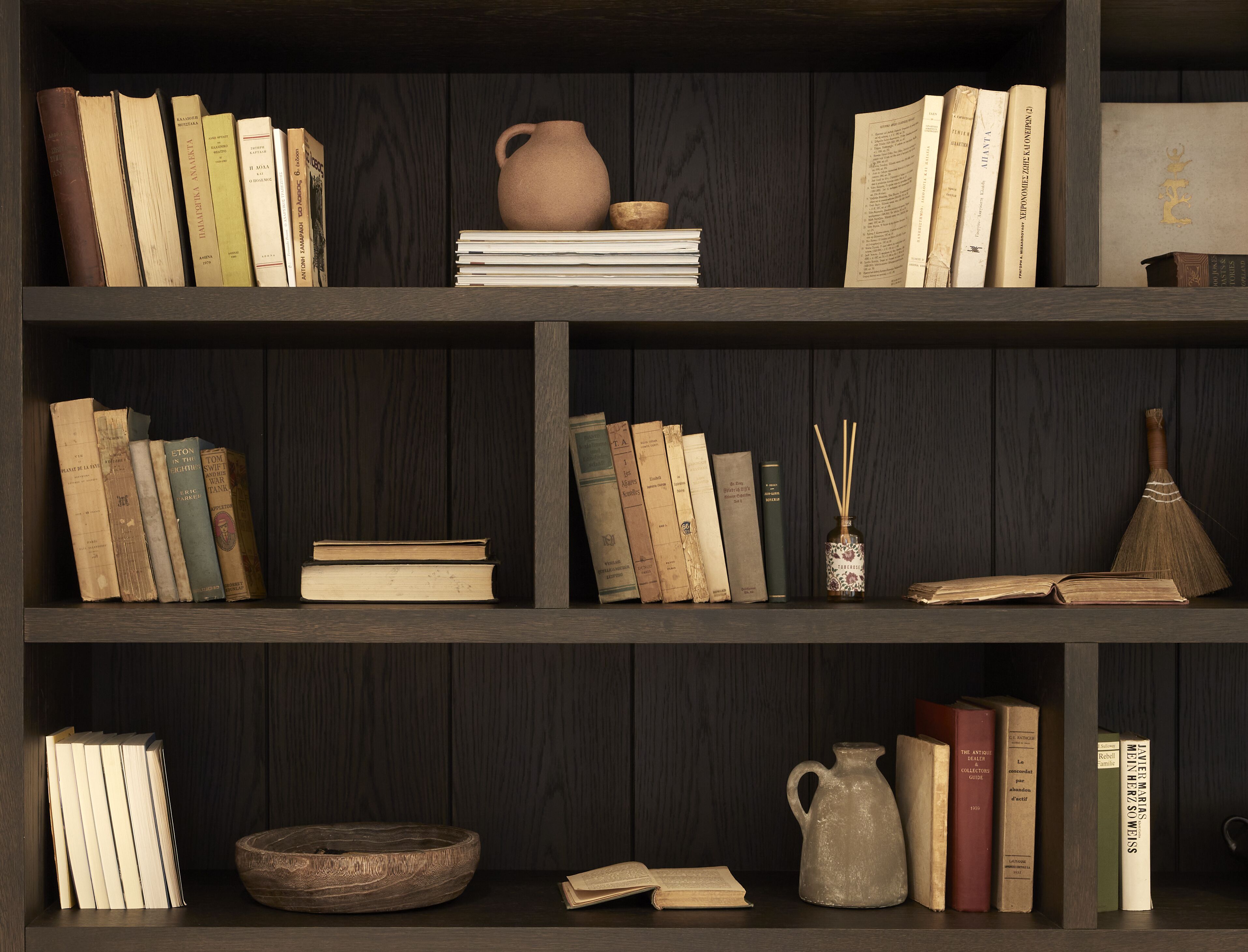 Uma estante com vários livros, um jarro de cerâmica e uma tigela de madeira.