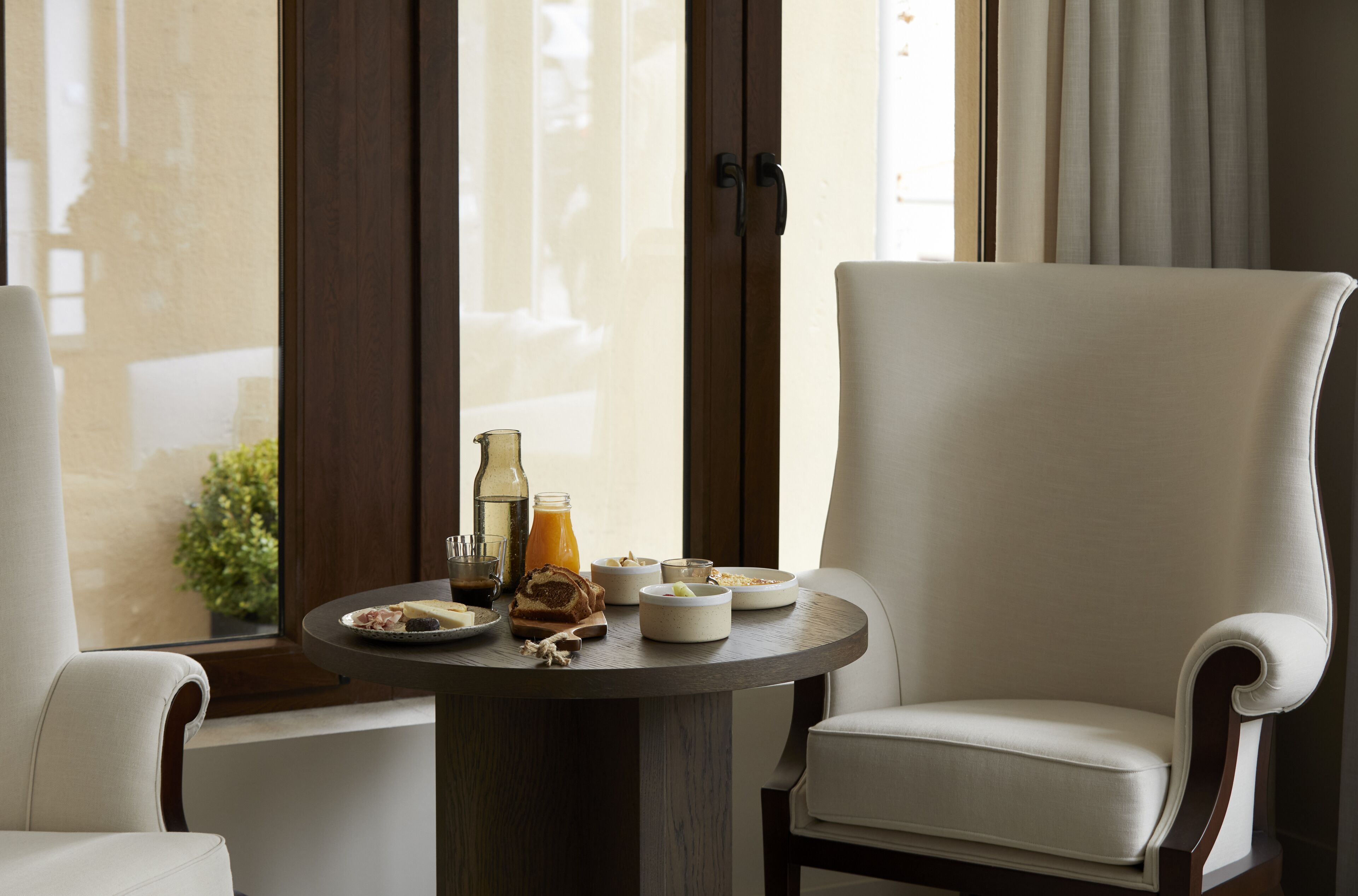 Un área de comedor con una mesa redonda dispuesta para el desayuno, con platos, tazones y una botella. Dos sillas tapizadas se encuentran alrededor de la mesa.