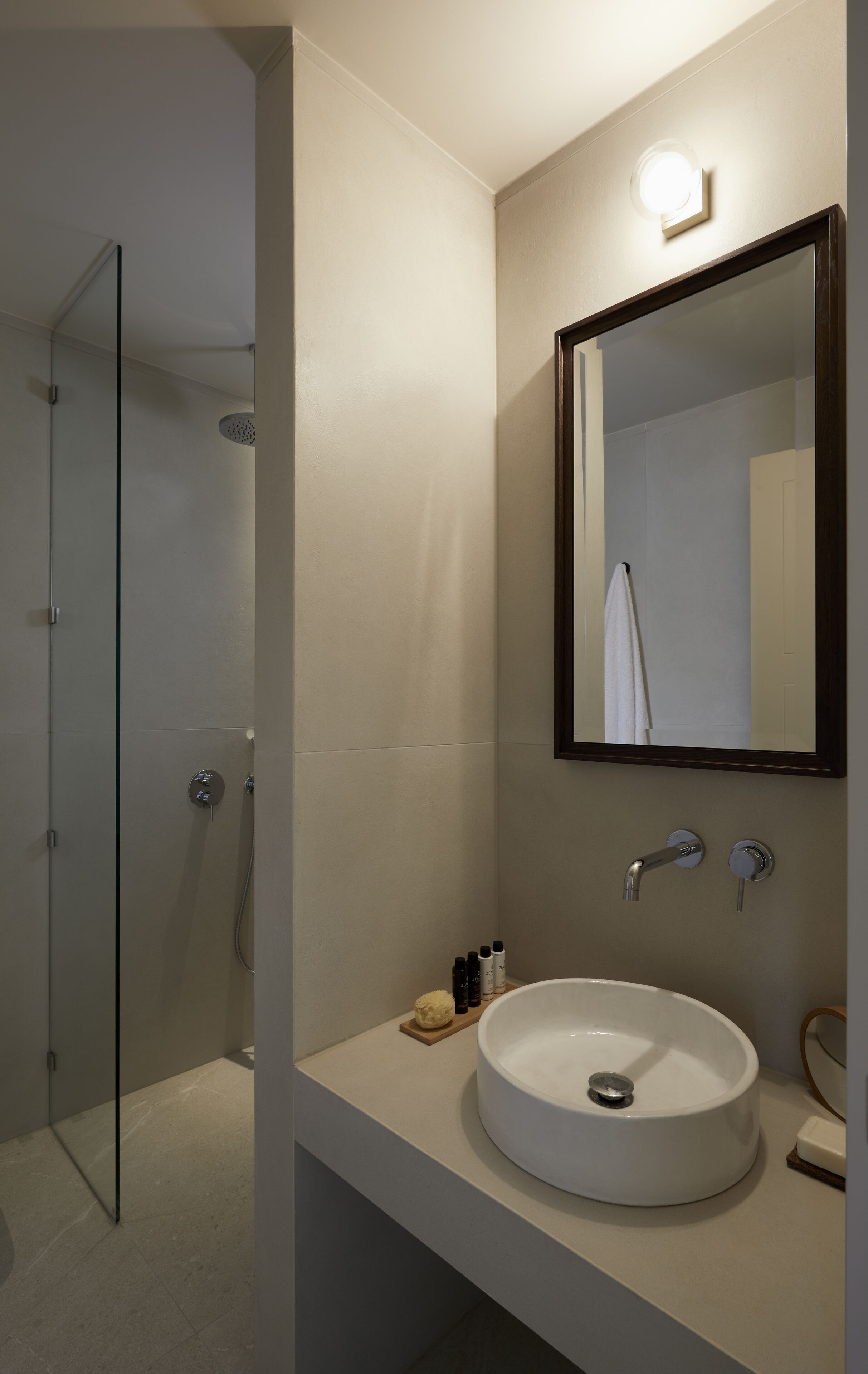 A modern bathroom with a glass shower enclosure, a white sink, and a mirror with a wooden frame.