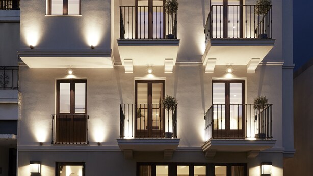 A multi-story building with balconies, large windows, and exterior lighting. - The Storyteller House (Kalabaka)