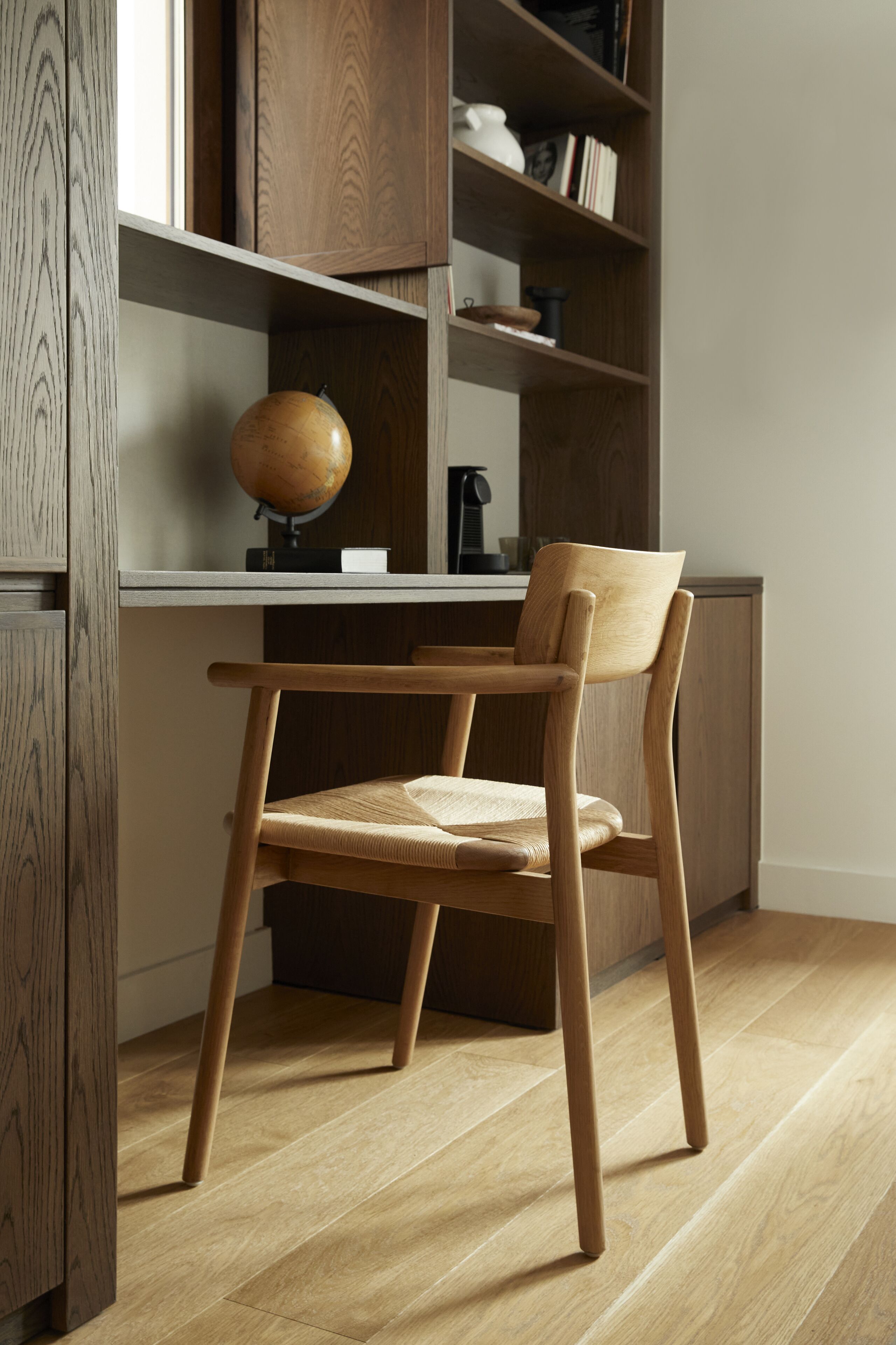 Een houten stoel met een geweven zitvlak en rugleuning, geplaatst voor een houten bureau met een wereldbol en een kop.