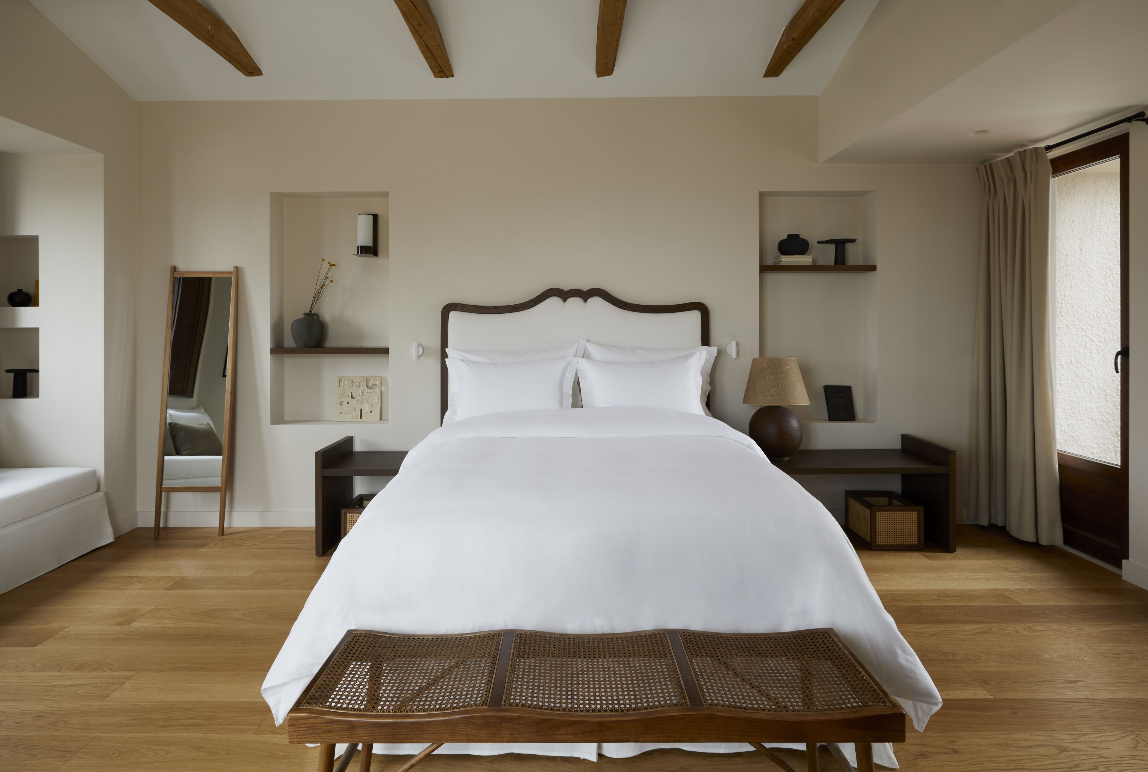 Un dormitorio ordenado con una cama grande, mesitas de noche, una silla y un espejo.