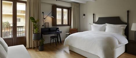 Habitación de hotel moderna con una cama grande, un escritorio con una silla, una planta en maceta y vistas al balcón exterior.