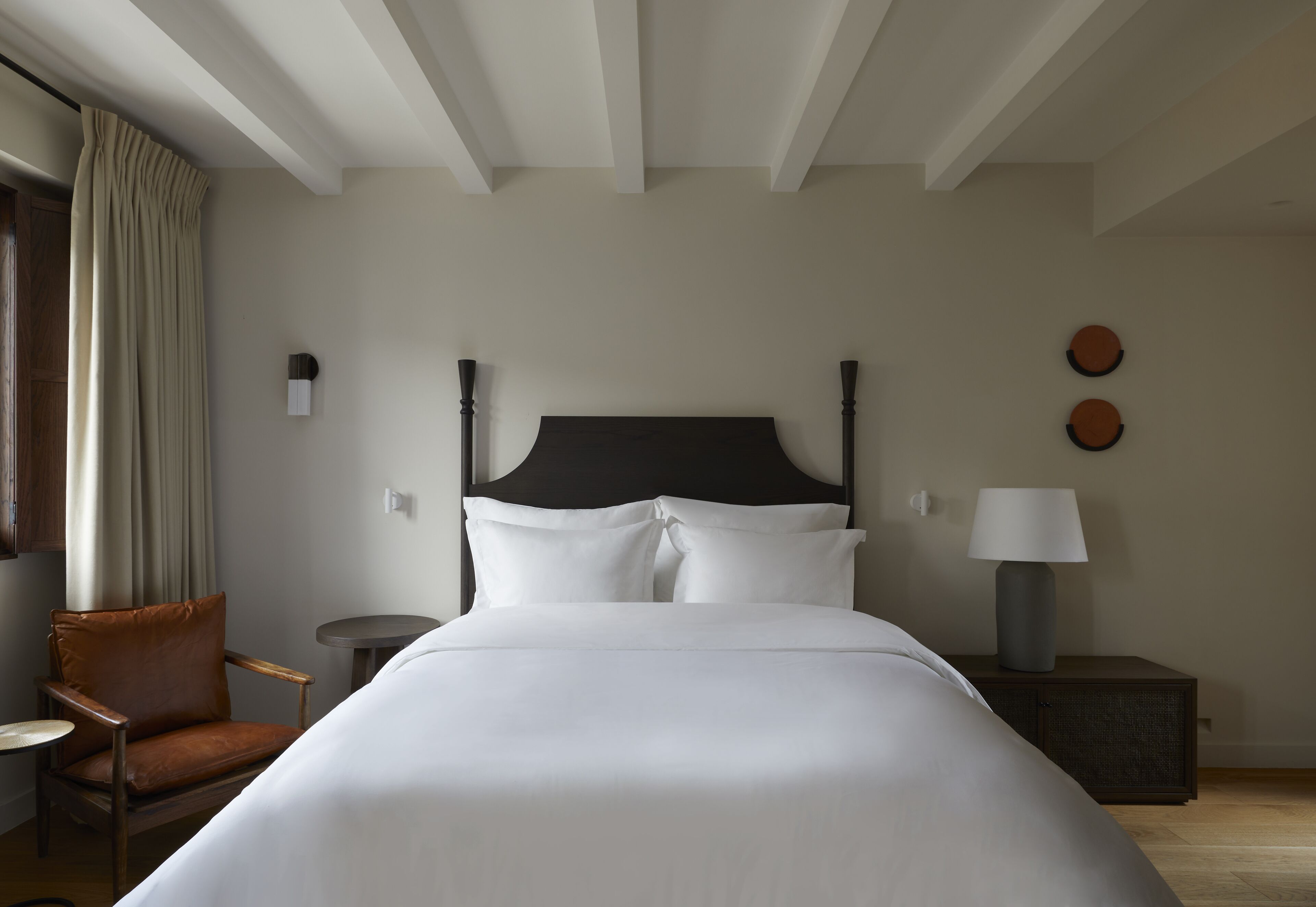 A hotel room with a large bed, a chair, a small table, and a lamp.