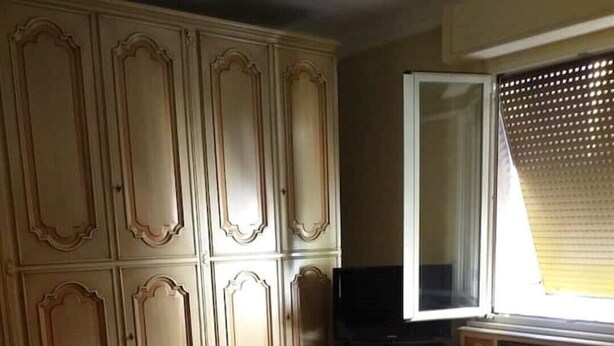 Ein Schlafzimmer mit großem Kleiderschrank, einem Bett und einem ordentlich gefalteten Handtuch, sowie einem Fenster mit Jalousien.