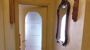 Ein schmaler Flur mit einer Tür am Ende, einem großen Spiegel an der Wand und einer kleinen Holzskulptur.
