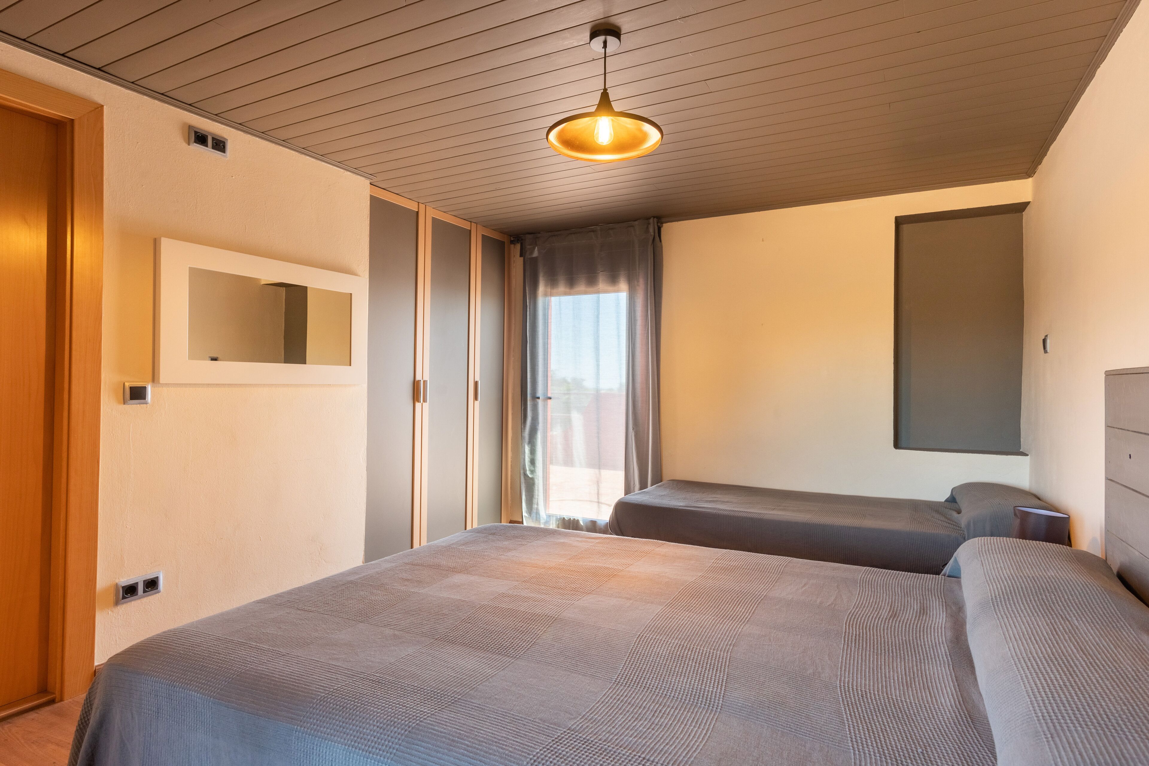 A hotel room with two beds, a wooden ceiling, a large mirror, and a window with curtains.
