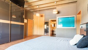 A modern bedroom with a large bed, a TV mounted on the wall, and a view of the kitchen. - Finca Escalicha (Cambrils)