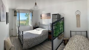 Un dormitorio con cama, una ventana con vistas, una mesita de noche y una estantería en la pared.