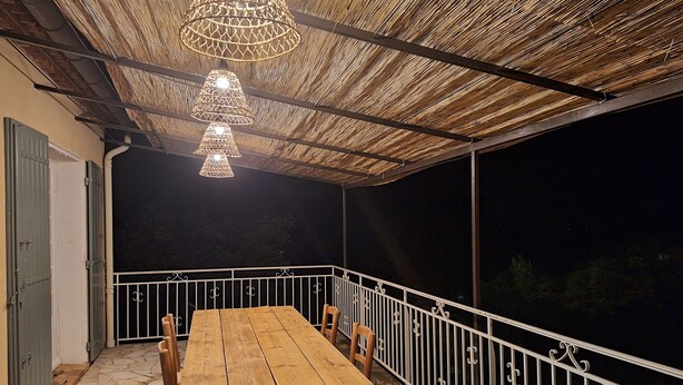 An outdoor patio with a wooden table and chairs, a thatched roof, and a white railing.