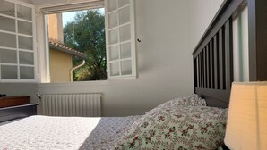 A bedroom with a bed, a window, a radiator, and a bedside table.