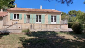 A two-story house with a tiled roof, green shutters, and a small balcony.