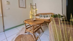 Una habitación con un sofá de mimbre, una pequeña mesa de comedor y una escalera en la pared.