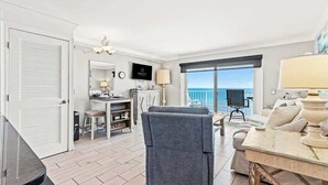 Amplia sala de estar con un gran ventanal con vista al mar, una mesa de comedor con sillas, un sofá y un televisor montado en la pared.