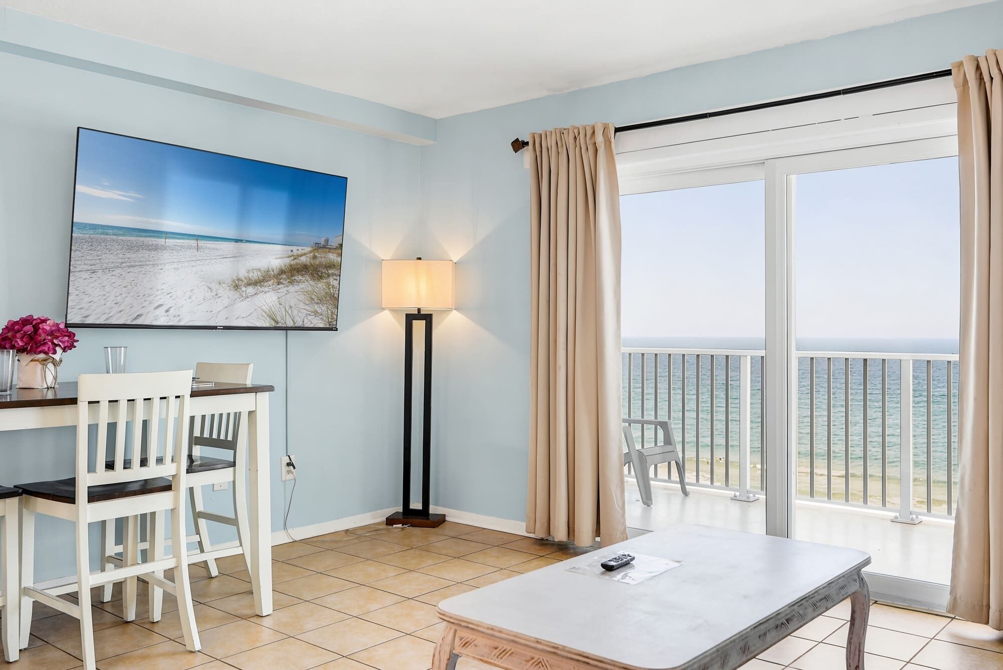 A room with a beach view, a desk with a chair, a lamp, and a table.