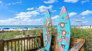 Twee surfplanken op een houten terras, met een strand op de achtergrond.