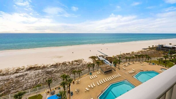 Un resort en la playa con zona de piscina, sillones de descanso y vista al océano.