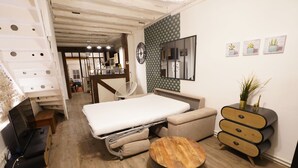 A compact bedroom with a bed, bedside table, and a small wooden stool. A dresser with drawers is against the wall, and a mirror hangs above it.