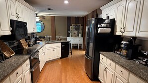 A kitchen with white cabinets, a black refrigerator, a granite countertop, and a wooden floor. - Georgia's Nature Retreat on Old Mill Pond (Statesboro)