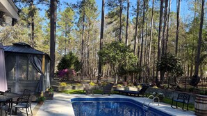 A pool area with a pergola, lounge chairs, and a view of tall trees. - Georgia's Nature Retreat on Old Mill Pond (Statesboro)