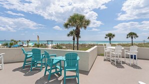 A rooftop terrace with turquoise chairs and tables overlooking a beach with umbrellas and palm trees. - Top Of The Gulf 111 - Ground Level Studio (Panama City Beach)