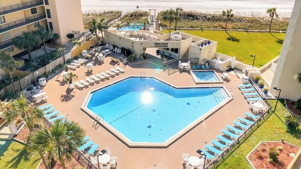 A hotel with a large pool surrounded by lounge chairs and palm trees, overlooking a beach. - Top Of The Gulf 111 - Ground Level Studio (Panama City Beach)
