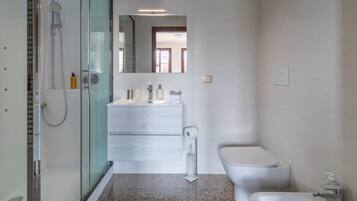 Ein modernes Badezimmer mit Duschkabine aus Glas, einem weißen Waschbecken mit Spiegel darüber und einer Toilette.