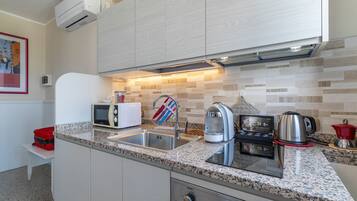 Cocina compacta con encimera de granito, microondas, hervidor, cafetera y pileta.