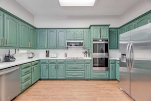 A kitchen with teal cabinets, stainless steel appliances, and a white countertop. - Boho Chic Home w Backyard Paradise - Pool + Grill (North Richland Hills)