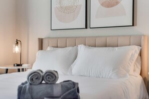 A neatly made bed with white linens, a headboard, and two framed abstract wall art pieces. - Boho Chic Home w Backyard Paradise - Pool + Grill (North Richland Hills)