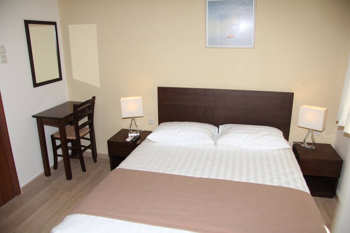 A hotel room with a bed, bedside tables, a chair, a desk, and a framed picture on the wall.