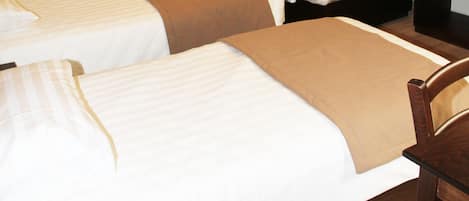 Une chambre d’hôtel avec deux lits simples, une chaise en bois, une petite table et un climatiseur fixé au mur.
