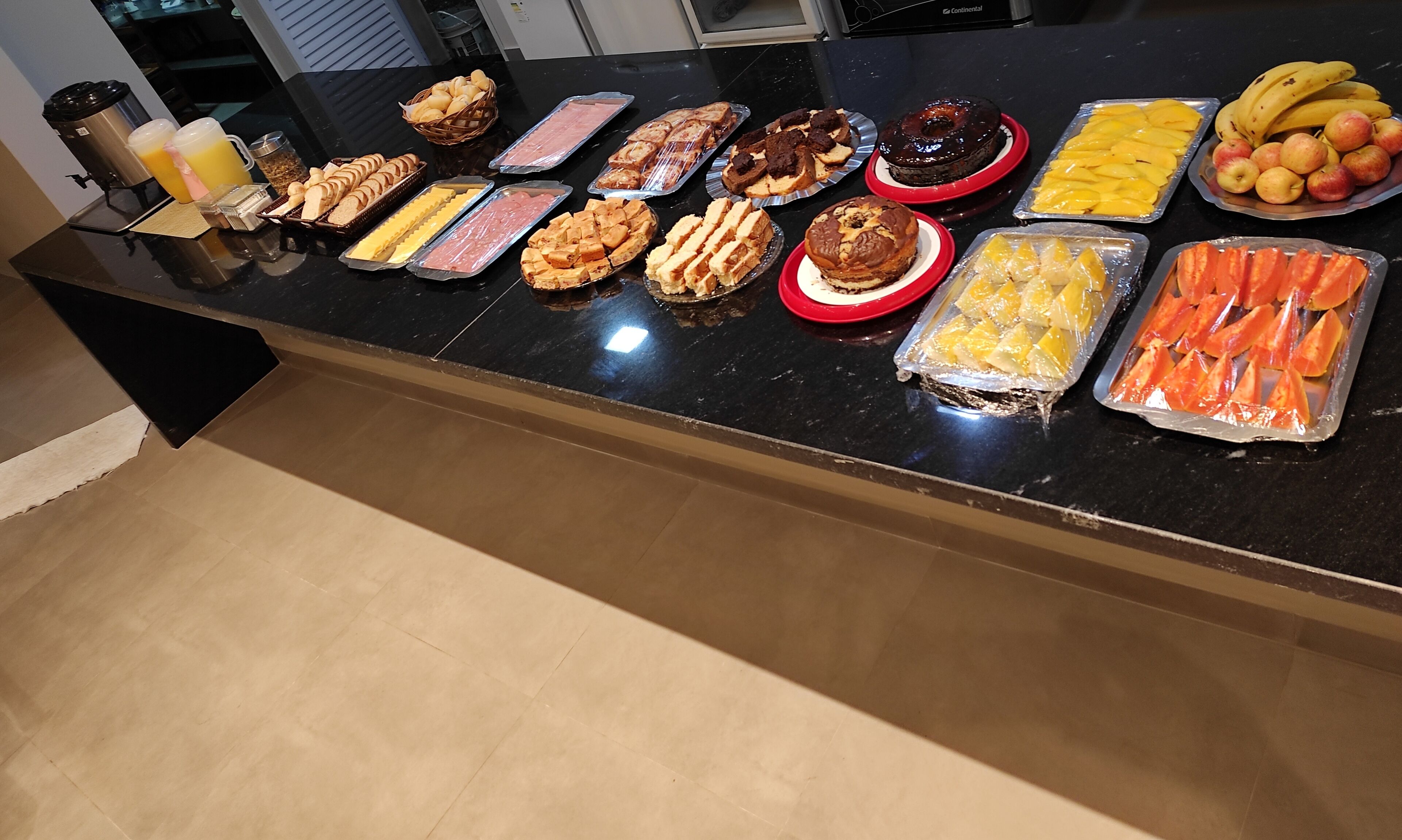 A buffet table with various food items including bread, cheese, meats, desserts, and fruits.