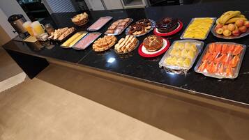 A buffet table with various food items including bread, cheese, meats, desserts, and fruits.