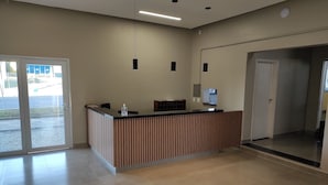 A reception area with a wooden reception desk, a glass dispenser, and a flat-screen TV. There are two pendant lights hanging from the ceiling.