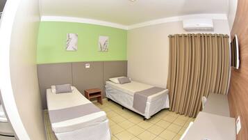 Habitación de hotel con dos camas individuales, una mesita pequeña, un escritorio con un control remoto y una ventana con cortinas.