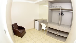 A room with a brown leather chair, a white chair, a desk, and a built-in wardrobe with shelves and hanging space.