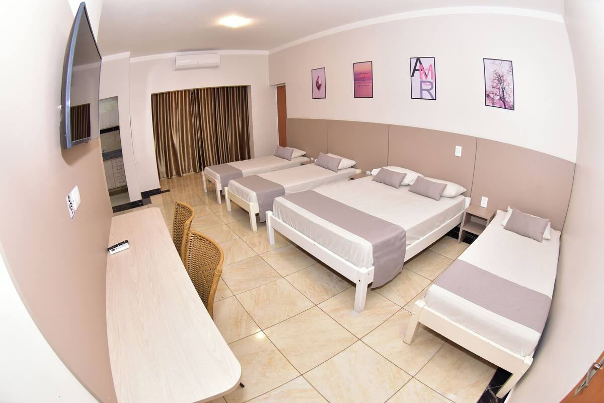 Una habitación de hotel con cuatro camas individuales, un escritorio, una silla y un televisor.