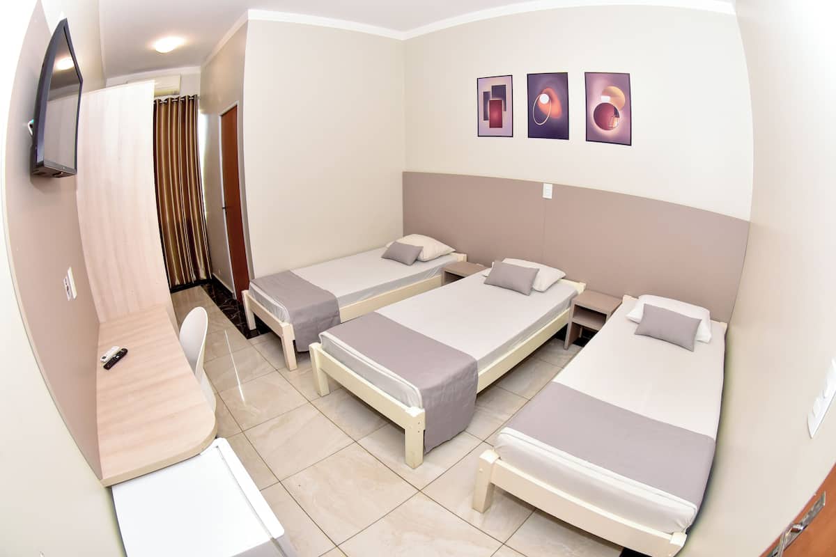 Habitación de hotel con tres camas individuales, un escritorio, una silla y un televisor montado en la pared.
